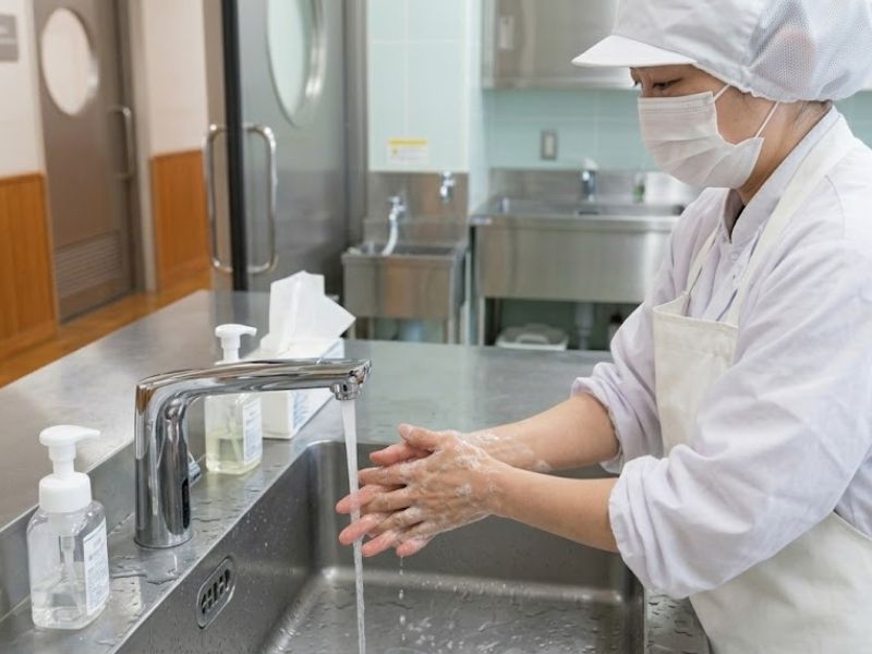 衛生管理を徹底するため、白い制服を着たスタッフが洗面台で石鹸を泡立てて念入りに手を洗っている手元のアップ。